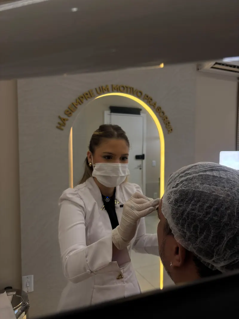 Dra. Letícia refletida no espelho com o arco iluminado do consultório
